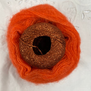 Ball of metallic orange yarn nestled inside a skein of orange brushed alpaca and silk yarn.
