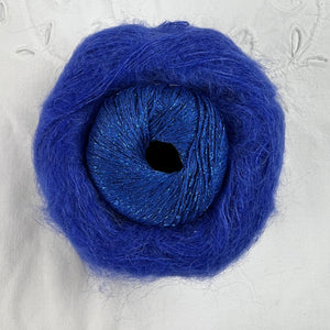 Ball of metallic royal blue yarn nestled inside a skein of royal blue brushed alpaca and silk yarn.
