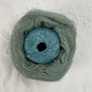 Ball of metallic aqua blue yarn nestled inside a skein of sage green brushed alpaca and silk yarn.
