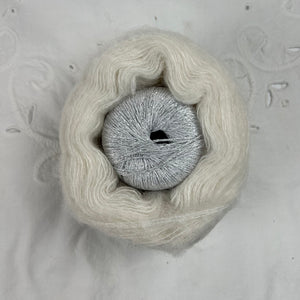 Ball of metallic silvery white yarn nestled inside a skein of white brushed alpaca and silk yarn.