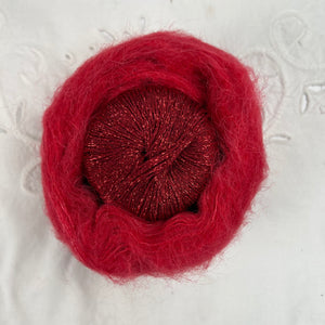 Ball of metallic red yarn nestled inside a skein of red brushed alpaca and silk yarn.