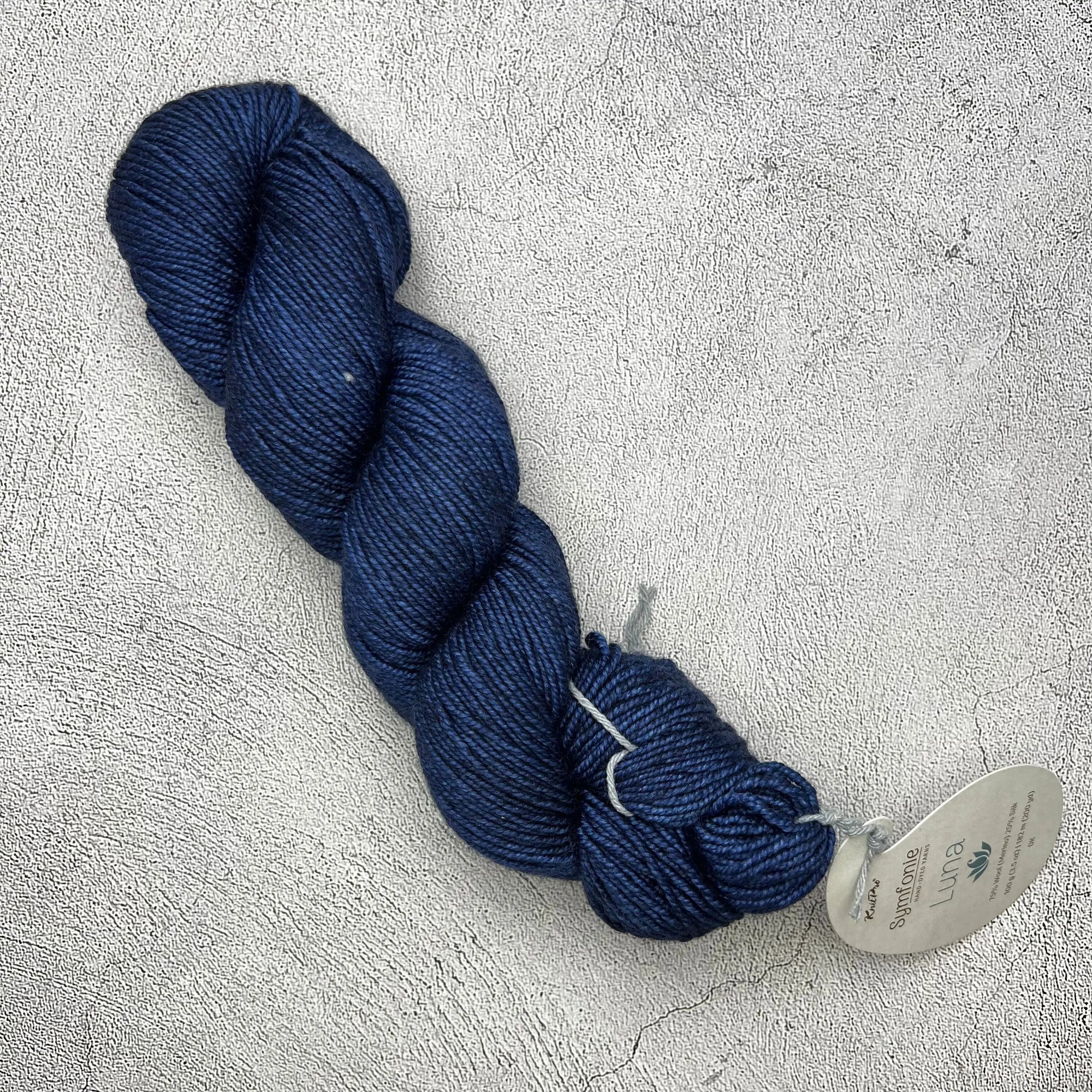 A skein of Knit Pro Symfonie Luna blue yarn on a concrete surface.